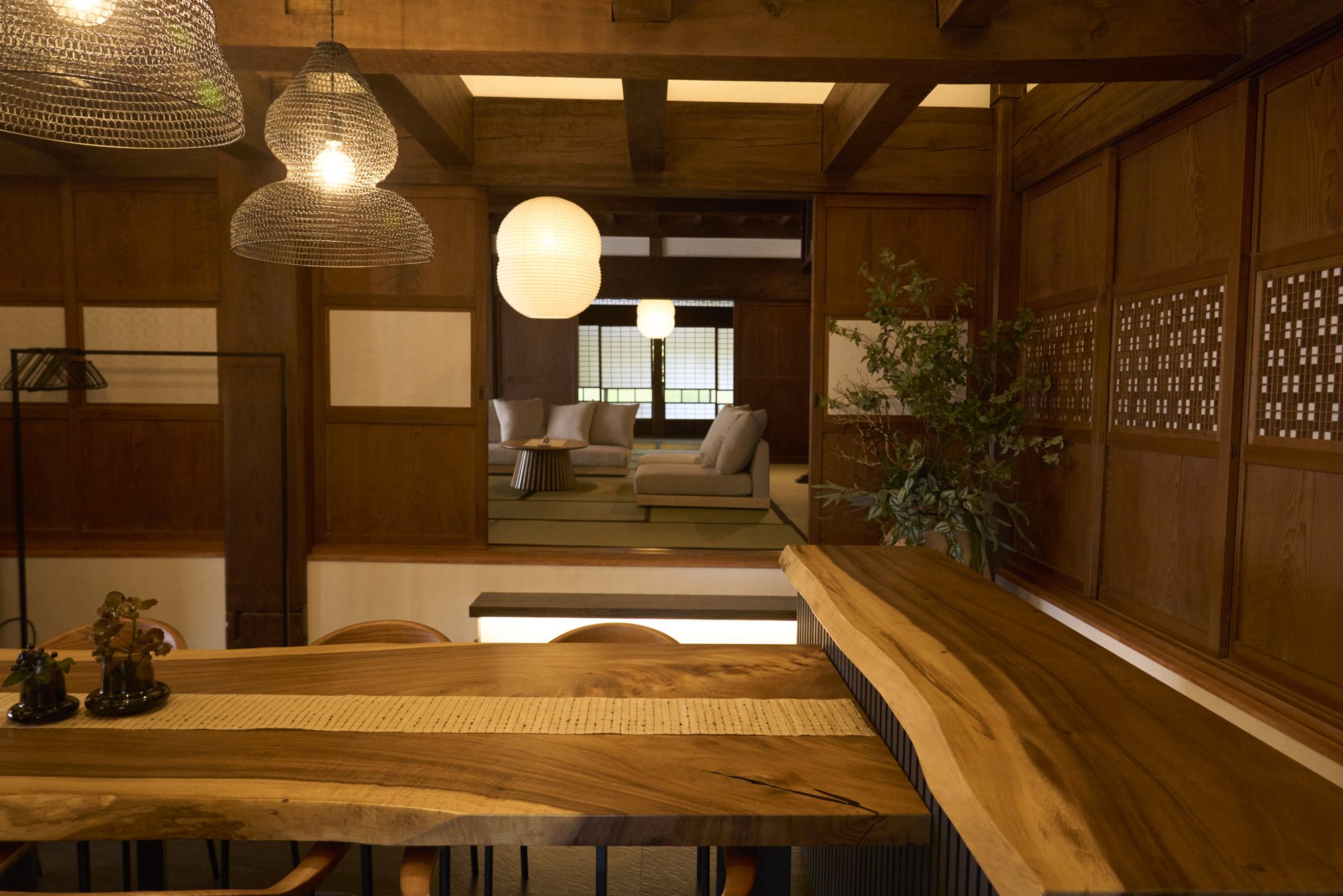 一枚板のテーブル越しに、一段下がった居間のソファへ視線が抜ける母屋の内観